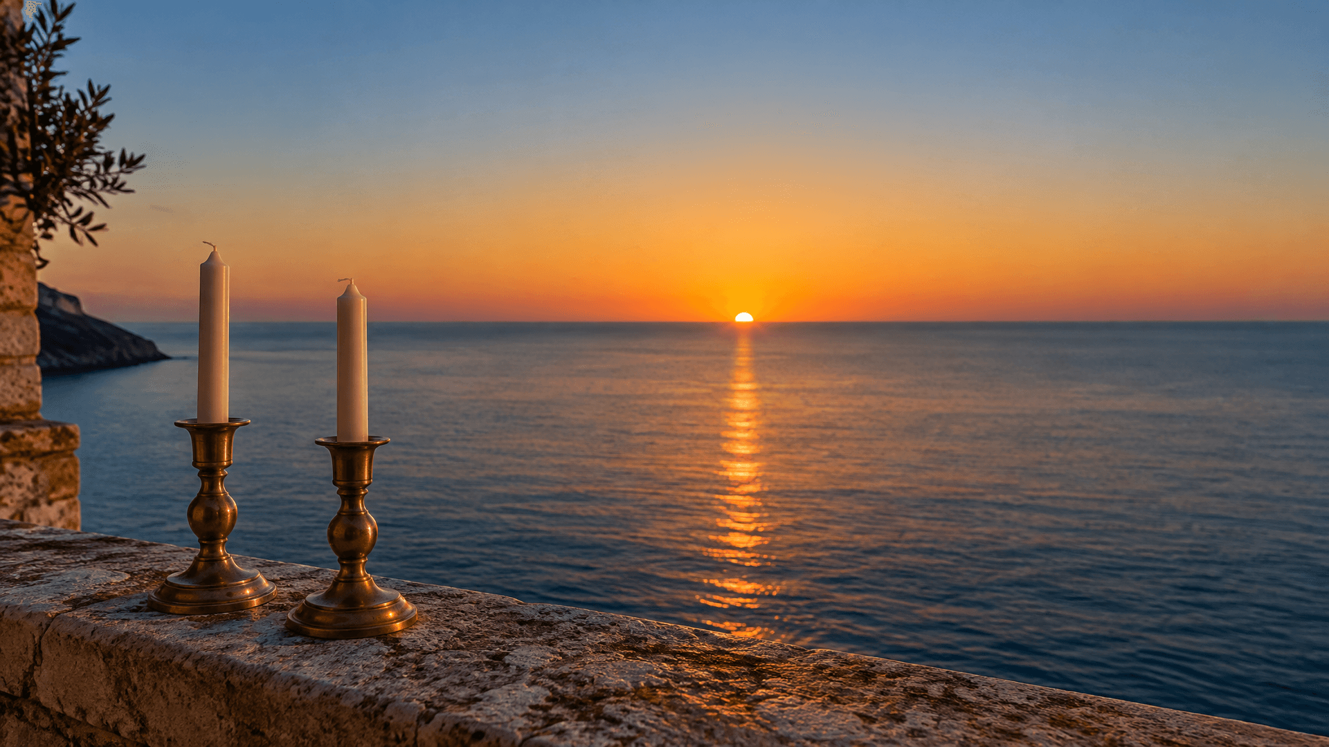 The sun sinks below a sea horizon; in the foreground, on a stone balcony ledge, two brass candlesticks hold candles that are not yet lit.